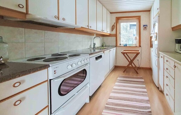 Eine kleine Küche mit weißen Schränken, einem Herd, einem Backofen und einem Fenster.
