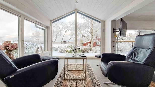 Ett modernt vardagsrum med ett stort fönster, två svarta läderfåtöljer, ett soffbord och en tv som är monterad på väggen.