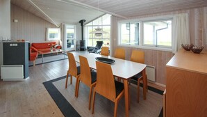 A cozy living room with a sofa, a dining table with chairs, a fireplace, and large windows. - Awesome home in Samsø with kitchen (Samsø)