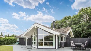 A modern house with a large glass extension, a covered patio, and a dining area with outdoor furniture. - Awesome home in Samsø with kitchen (Samsø)