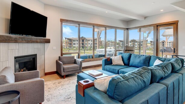 A spacious living room with a fireplace, a large blue sofa, a grey armchair, and a flat-screen TV.