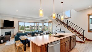 A modern kitchen with a central island, a dining area with a table and chairs, a sofa, and a staircase leading to an upper level.