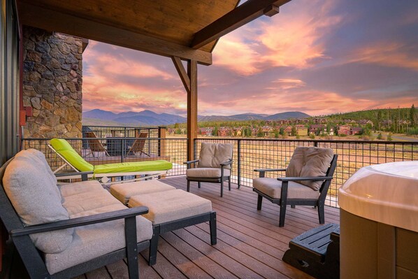 A wooden deck with outdoor seating, a stone wall, and a view of a residential area with houses and mountains in the background.