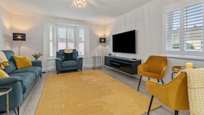 A modern living room with a sofa, armchairs, a TV, and a fireplace. - Cottage Mews - Seaside Cottage Parking Terrace (Tenby)