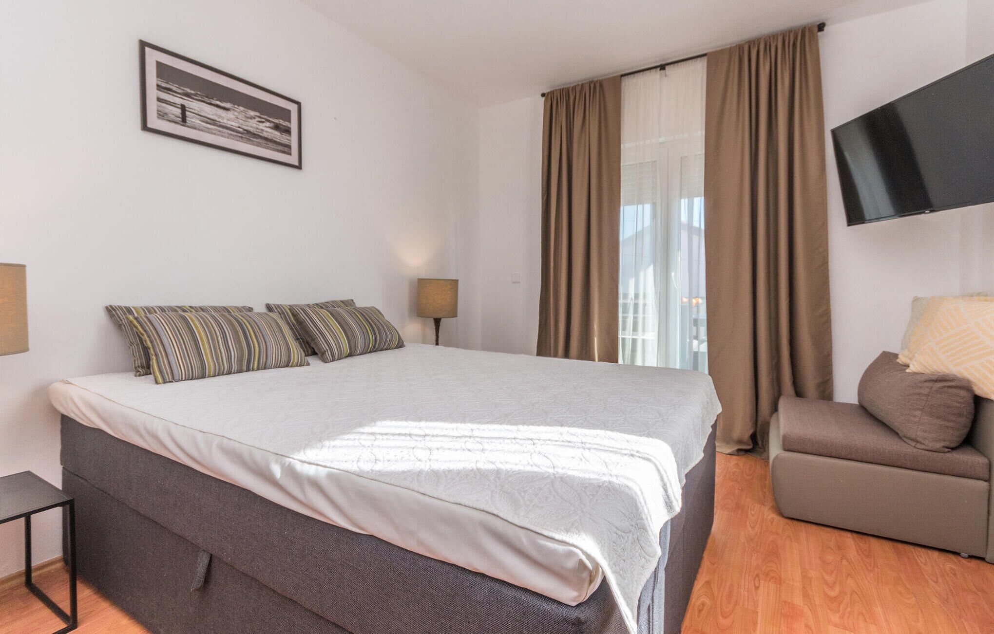 Una habitación de hotel con una cama grande, un sofá, un televisor montado en la pared y una ventana con cortinas.