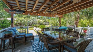 A covered outdoor patio with wicker furniture, a glass-top table, and a view of a lush garden. - Private Pool! Golf Cart! Bikes! 143 Beth Lane! (Santa Rosa Beach)