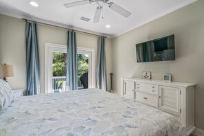 Ein Schlafzimmer mit einem großen Bett, einem Deckenventilator, einem an der Wand montierten Fernseher und einem Fenster mit Vorhängen.