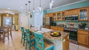 A kitchen with a central island, wooden cabinets, stainless steel appliances, and a dining area with chairs. - Private Pool! Golf Cart! Bikes! 143 Beth Lane! (Santa Rosa Beach)