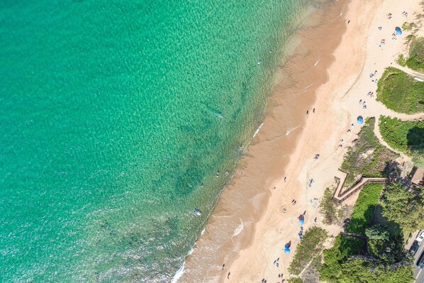 Vista aérea de una playa con agua turquesa cristalina, orilla de arena y gente disfrutando.