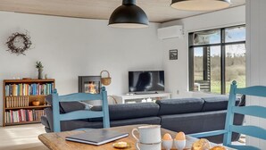 Moderni olohuone, jossa on sohva, televisio, kirjahylly ja ruokapöytä, jonka päällä on aamiaisruokia.