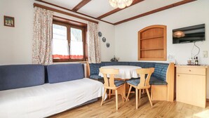 Een gezellige kamer met een bank, een eettafel met stoelen, een houten kast en een televisie aan de muur.