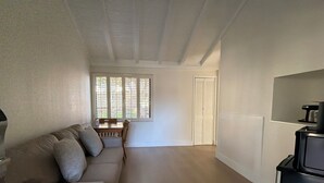 A compact living space with a sofa, a dining table, a TV, and a window with blinds.