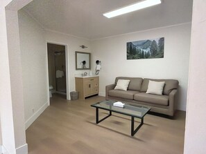 A living room with a beige sofa, a glass coffee table, a wooden cabinet, and a painting on the wall.