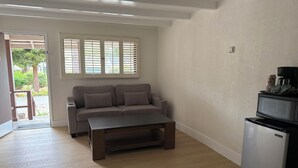 A living room with a sofa, coffee table, and refrigerator. - One Bedroom Suite Cottage (Carmel-by-the-Sea)