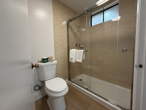 A bathroom with a toilet, a glass shower enclosure, and a towel rack. - One Bedroom Suite Cottage (Carmel-by-the-Sea)