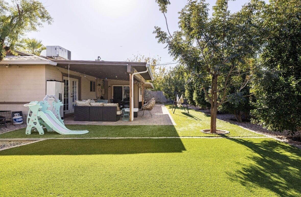 A residential backyard with a covered patio, a slide, and a lawn.