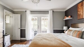Ein Schlafzimmer mit einem großen Bett, einem Deckenventilator, einer Tür und einem Fenster mit Vorhängen.