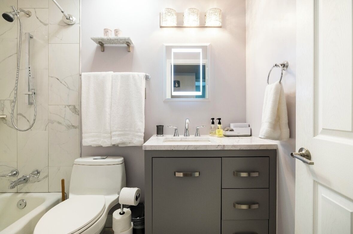 Une salle de bain équipée de toilettes, d’un lavabo et d’une douche. Des serviettes sont accrochées au mur et une étagère contient des articles de toilette.