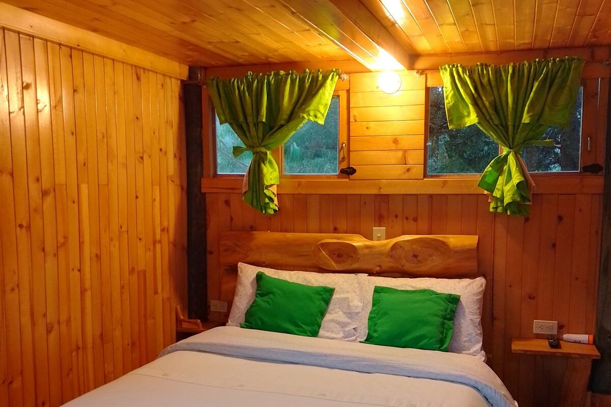 A wooden cabin bedroom with a bed, green curtains, and a nightstand.