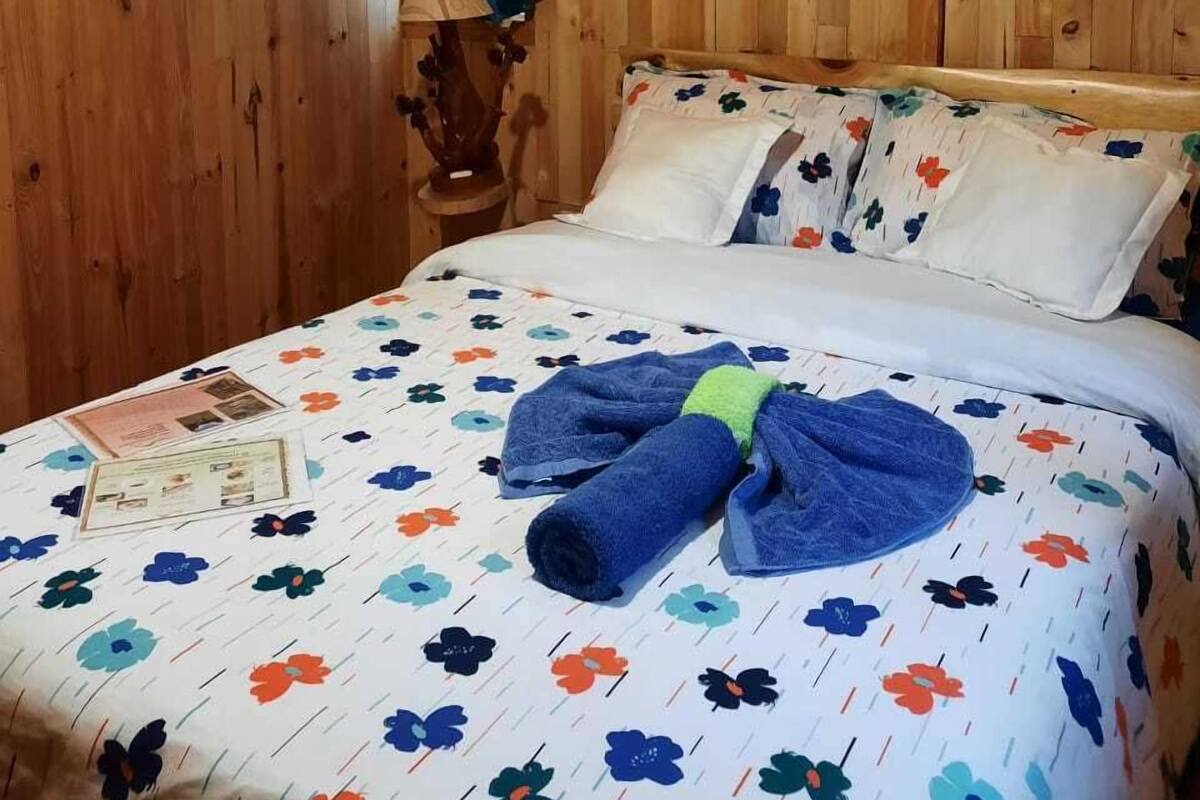 A wooden-paneled room with a bed featuring a floral bedspread, a blue towel, and a wooden headboard.