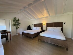 A hotel room with two beds, a desk, a chair, and a potted plant.