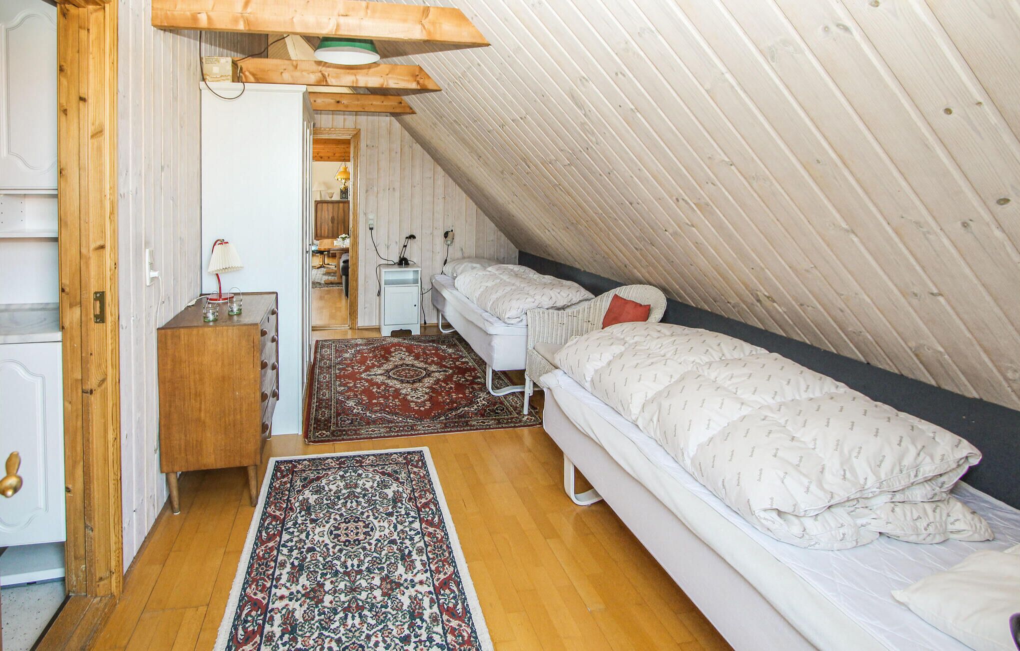 Un pequeño y acogedor dormitorio en el ático, con paredes de madera y techo inclinado, y una cama individual.