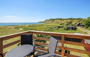 A wooden deck with a table and chairs overlooking a coastal landscape with a small building in the distance.
