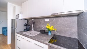 Eine moderne Küche mit weißen Schränken, einer Marmor-Spritzschutzwand, einem Einbauofen und einem Spülbecken.