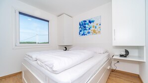Ein Schlafzimmer mit Bett, Fenster mit Aussicht, einem Gemälde und einem Schreibtisch mit Lampe.