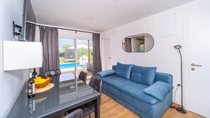 Ein modernes Zimmer mit einem Glastisch, einem blauen Sofa, einem großen Spiegel und Blick auf einen Swimmingpool.