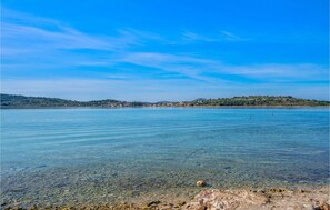 A clear view of a lake with a rocky shoreline and a distant shoreline with buildings. - 11 bedroom amazing apartment in Srima (Srima)