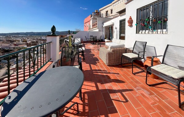 Una terraza con mesa y sillas, vista a la ciudad y un edificio blanco con una ventana decorada con luces de colores.