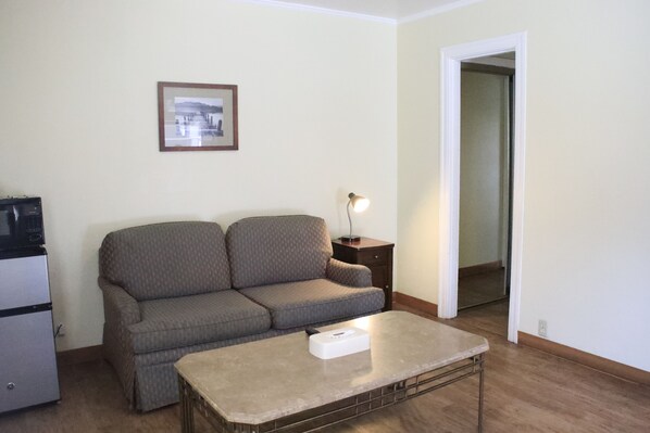 A living room with a sofa, a coffee table, a lamp, and a picture on the wall. - Two Queen Suite Cottage (Carmel-by-the-Sea)