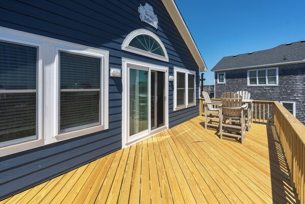 A deck with a wooden floor and two Adirondack chairs, a sliding glass door, and a window with a white frame.