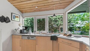 Una cocina moderna con armarios de madera, un lavavajillas Bosch, una cafetera y un ventanal con vistas al verdor.