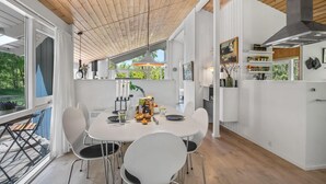 Una cocina moderna con armarios blancos, un comedor con mesa y sillas blancas, y techo de madera.