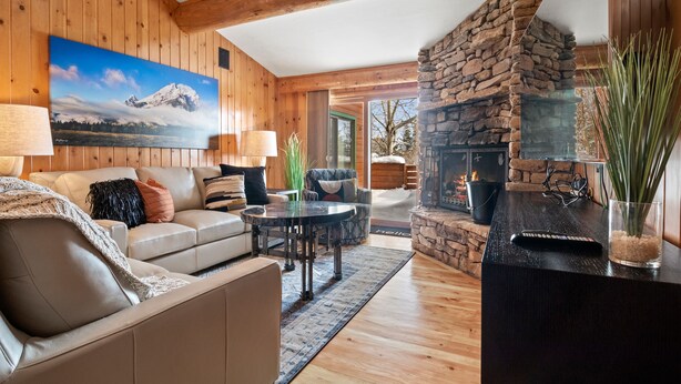 Una sala de estar acogedora con chimenea de piedra, paredes de madera y un cuadro grande de una montaña.