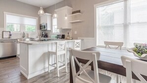 Une cuisine moderne avec des meubles blancs, un îlot central, des tabourets de bar et une table à manger avec des chaises.