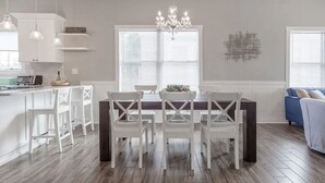 Une cuisine moderne avec des meubles blancs, une table à manger entourée de chaises blanches et un lustre.