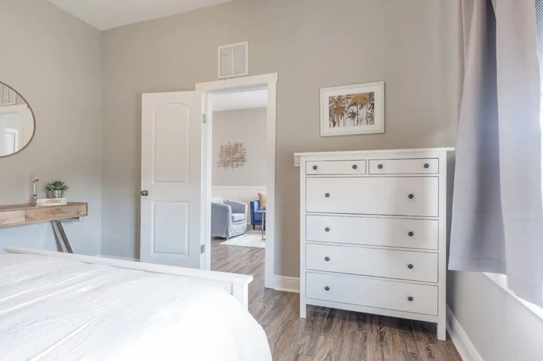 A bedroom with a bed, a dresser, a mirror, and a door leading to another room.