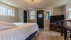 A bedroom with a bed, a TV, a wooden bench, and a door. - Cozy Cabin in a rural setting #12 in Temple NH (Temple)