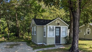 A small, single-story cabin with a dark front door and a mailbox, surrounded by trees and a gravel driveway. - Cozy Cabin in a rural setting #12 in Temple NH (Temple)