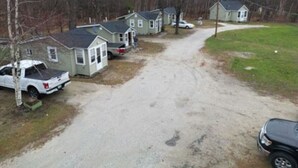 A residential area with multiple houses, a gravel driveway, and parked vehicles. - Cozy Cabin in a rural setting #12 in Temple NH (Temple)