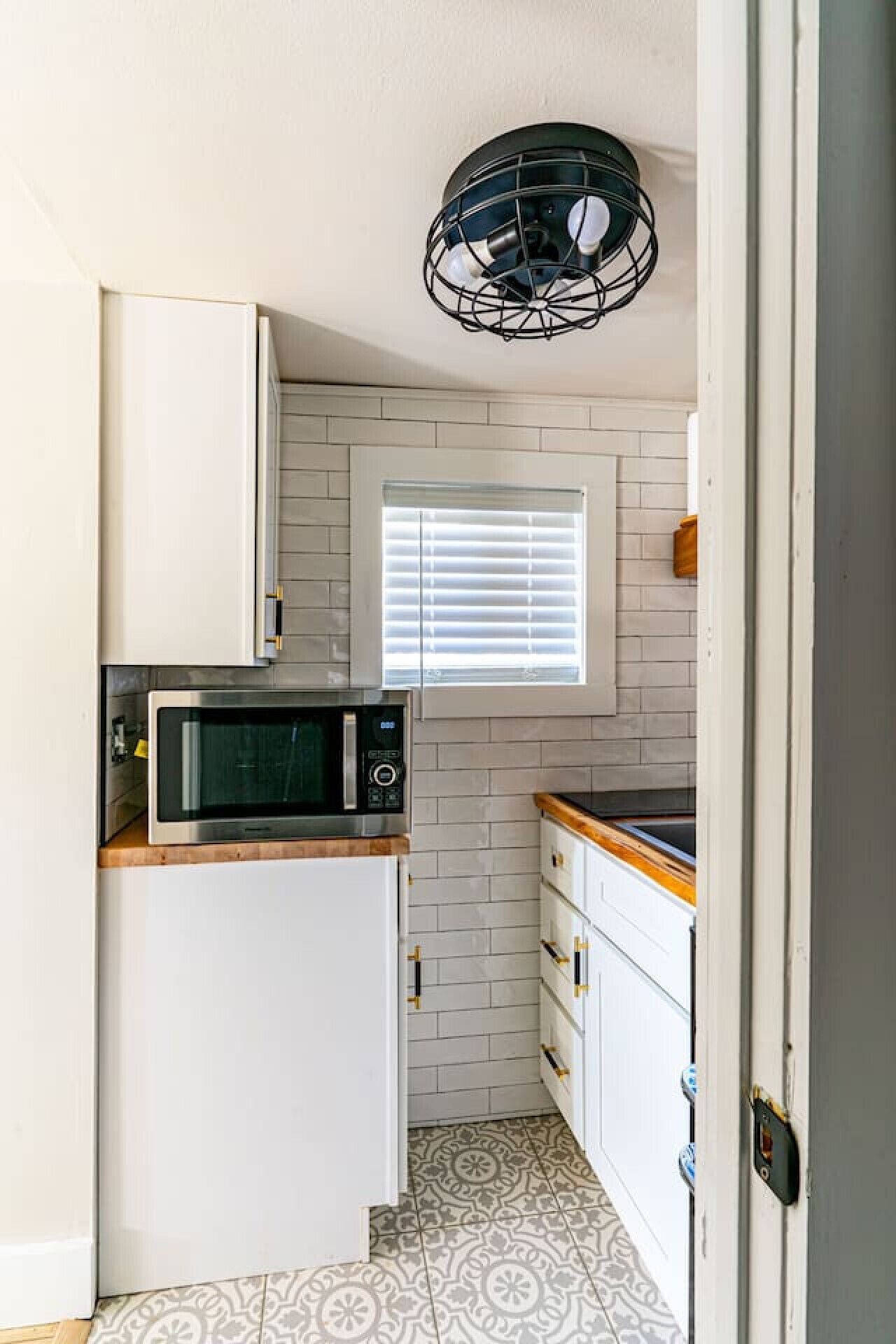 A compact kitchen with white cabinets, a microwave, and a window with blinds.