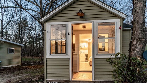 A small, single-story house with a front door open, revealing a kitchen area with a sink and cabinets. - Cozy Cabin in a rural setting #12 in Temple NH (Temple)