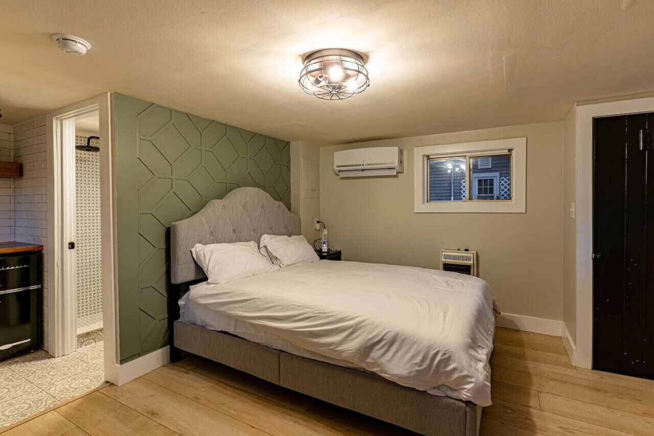 A bedroom with a bed, a nightstand, a window, and an air conditioning unit.
