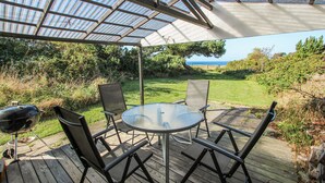 En uteplats med ett glasbord och stolar, en grill och utsikt över havet.