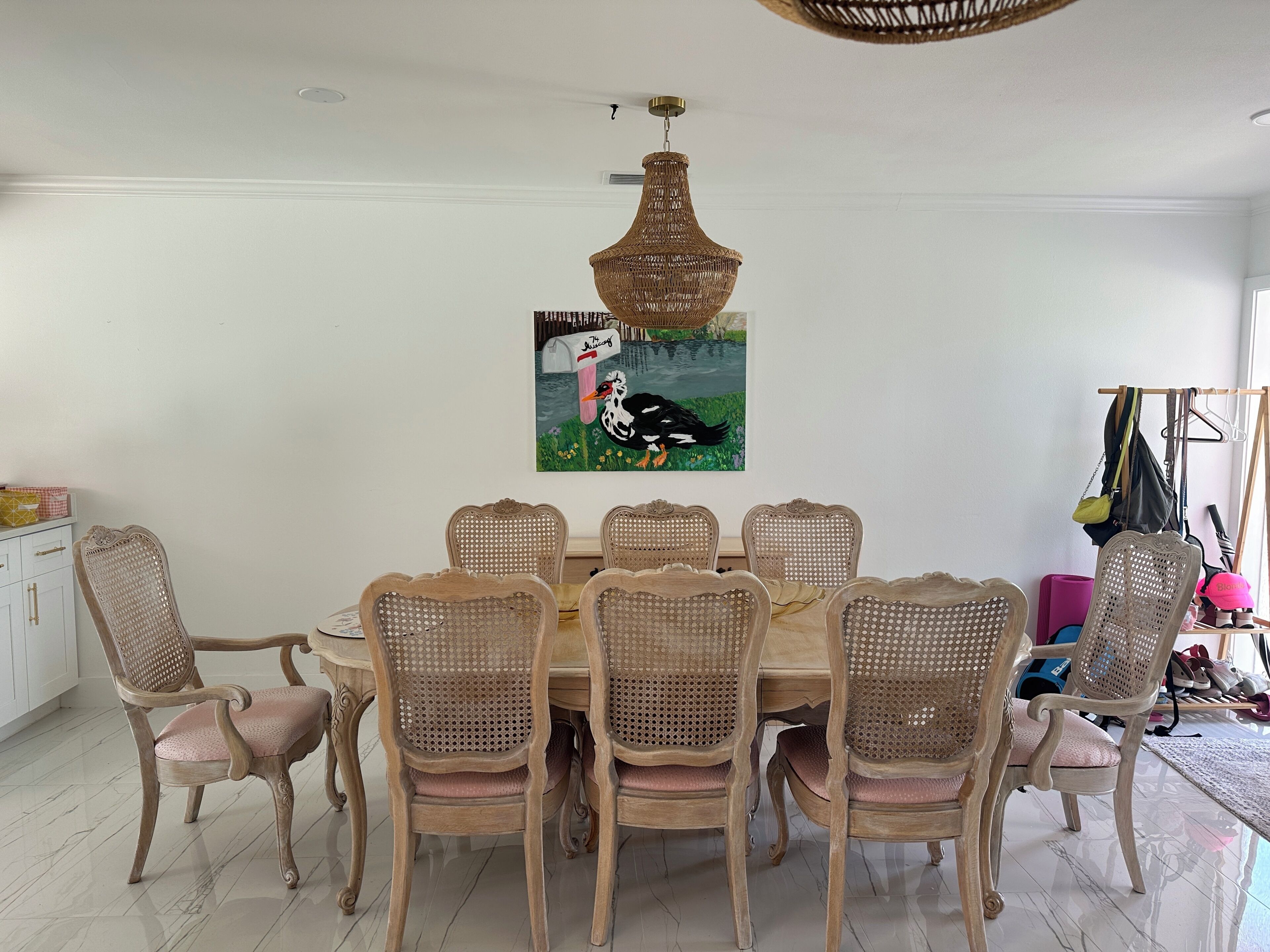 A dining area with a round table, six chairs, and a hanging wicker chandelier.