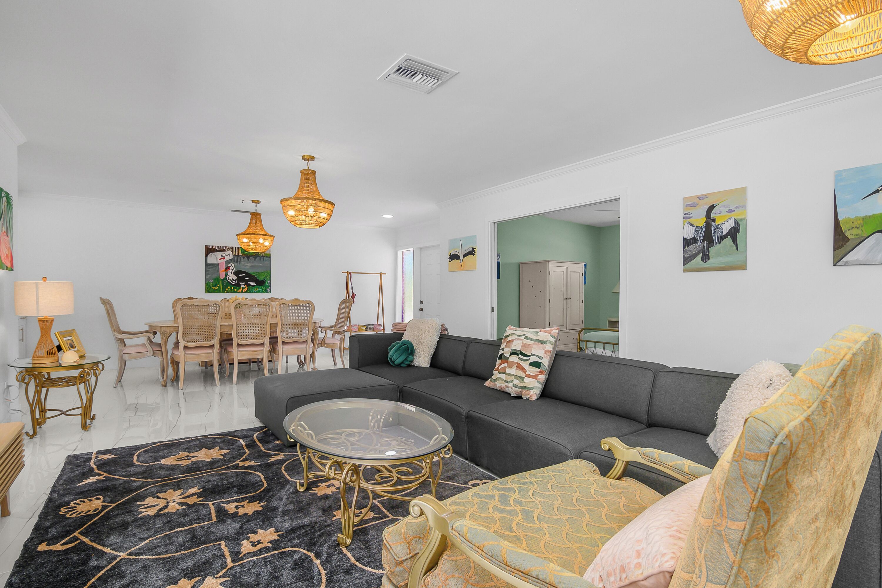 A living room with a sofa, armchairs, a glass coffee table, a dining area with chairs, and a chandelier.