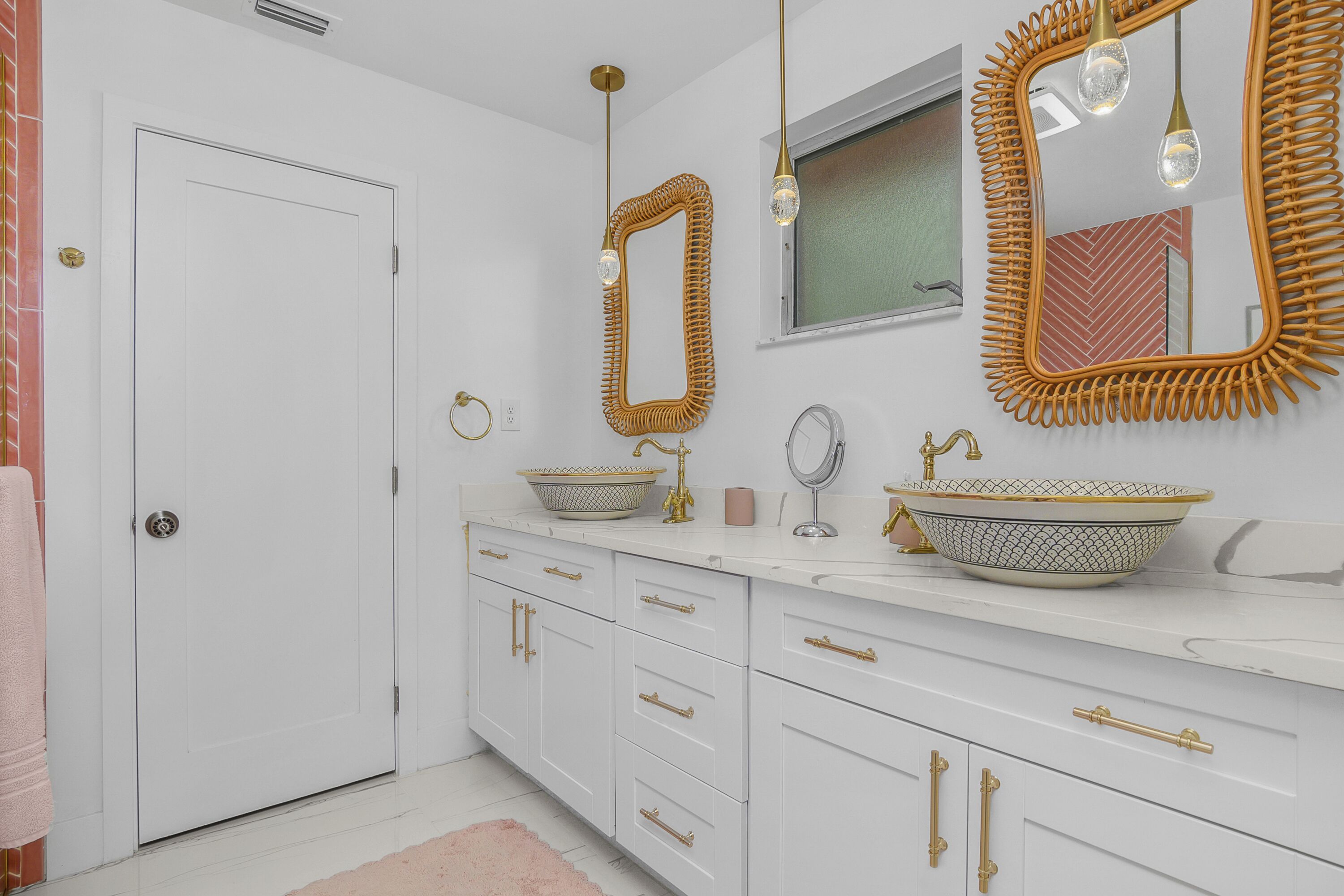 Een badkamer met witte kastjes, gouden details en een grote spiegel met een rieten lijst.